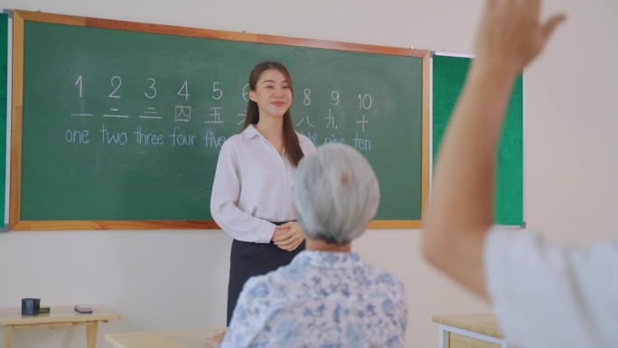 亚洲女教师在语言学校教成人学生。有魅力的女老师在家教课上讲解和激励老年老人学习新技能。