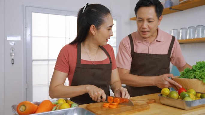 一对亚洲夫妇在厨房里互相帮助切菜和做饭。这个概念强调了家庭内部的关系。