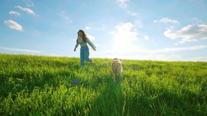 无忧无虑的年轻女子和可爱的金毛猎犬在晴朗的蓝天下的草地上奔跑