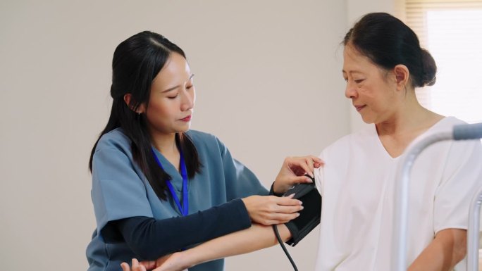穿着蓝色工作服的亚洲护理护士给坐在卧室床上的老年妇女检查血压监测仪和带数字压力表的心率监测仪，医疗保