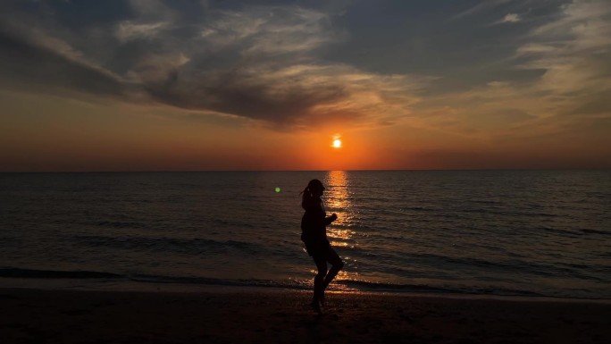 一个女孩的剪影在沙滩上奔跑，背景是夕阳和大海的地平线