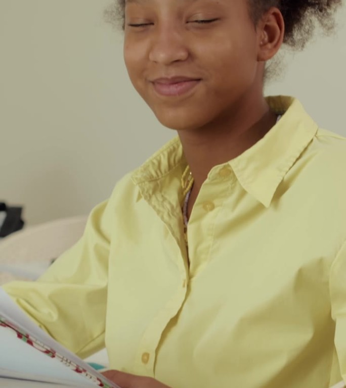 微笑的青少年黑人女孩坐在书桌前拿着教科书的肖像