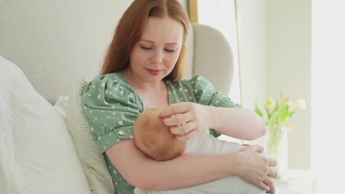 家庭美满。母亲母乳喂养婴儿有利于健康营养养生。妈妈在家给刚出生的孩子喂奶。白色卧室里的女婴儿，母亲充