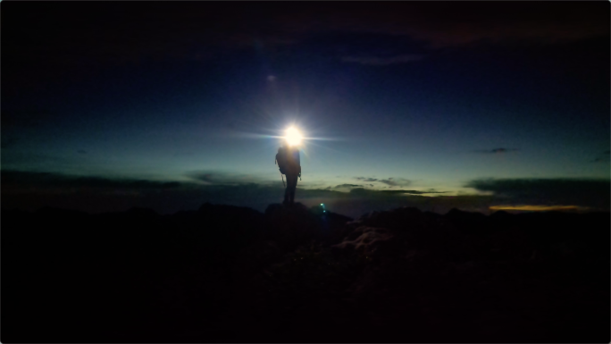 夜里登顶山峰的探险家打着电筒照亮前行的路