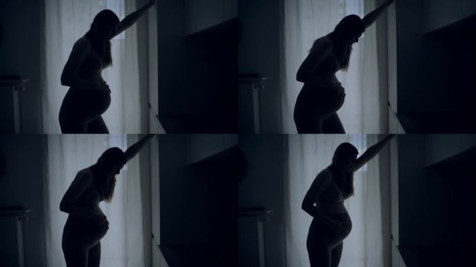 孕妇临产的剪影。她疼了，摸了摸肚子。