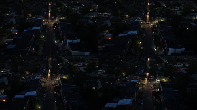 美国城市十字路口的夜景。街道两旁是排屋和昏暗的街灯。汽车的前灯在道路上形成光迹。天线。