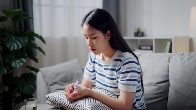 年轻的亚洲女子正在家里舒适的沙发上服药。