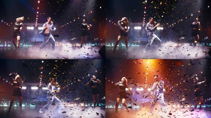 穿着休闲服装的充满活力的流行艺术家与两名穿着另类服装的年轻女舞者在舞台上表演。激动的观众被充满活力的