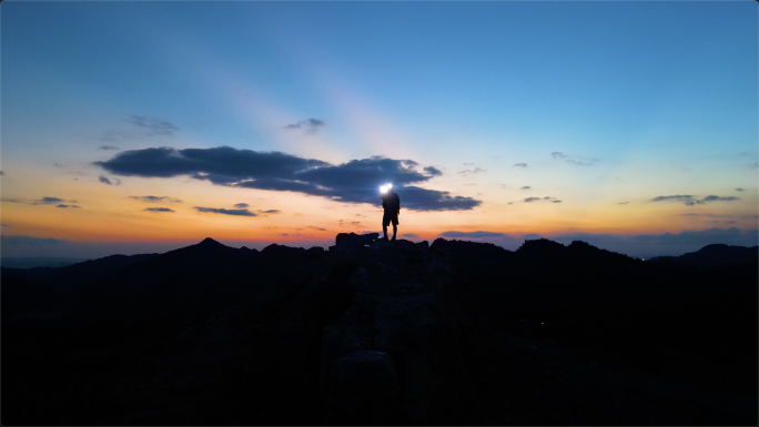 探险家黑夜登顶山顶打着手电筒照亮前行的路