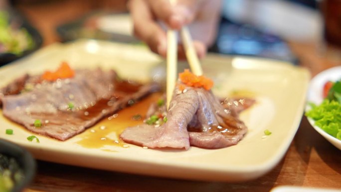 (特写)在日本餐厅用筷子夹起桌上的热烤肉。