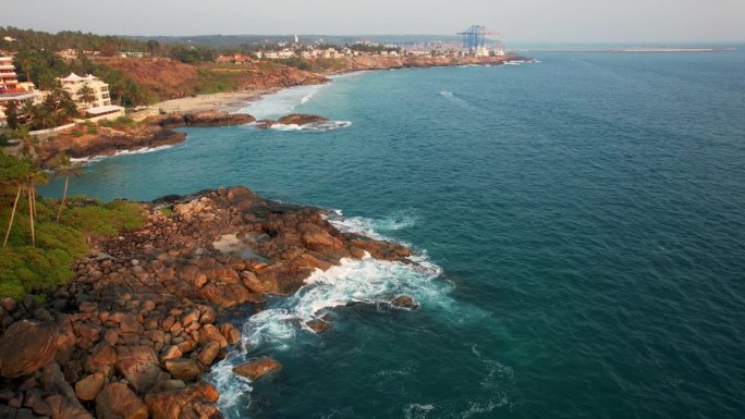 鸟瞰碧绿的海浪撞击岩石海岸线，大海在布满巨石的海岸线周围编织。Kovalam海滩，印度喀拉拉邦。