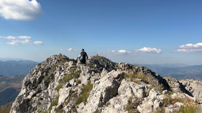 一个背着背包的游客在阳光照耀下沿着高高的岩石山脊行走，背景是美丽的山脉全景