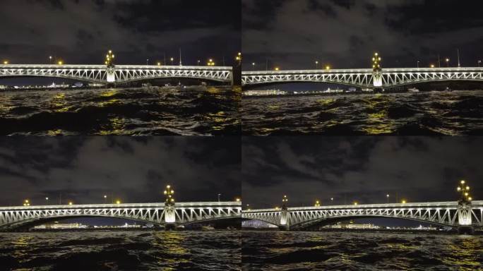 河上一座灯火通明的桥的夜景，下面有船只经过