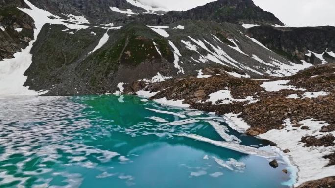 被雪崩袭击的高山湖泊当地的高原湖泊，在阴天被陡峭的山峰包围。鸟瞰图