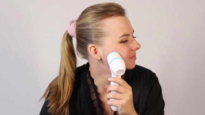 30多岁的女人用面部按摩器按摩自己的脸。面部护理