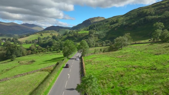 夏日里，车辆行驶在远山的乡间小路上。英国坎布里亚郡湖区国家公园