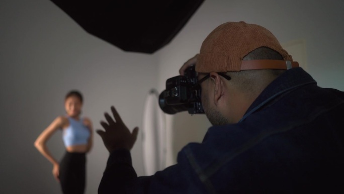 专业男摄影师使用数码相机和闪光灯在白色背景的摄影棚内拍摄女模特。摄影的概念。