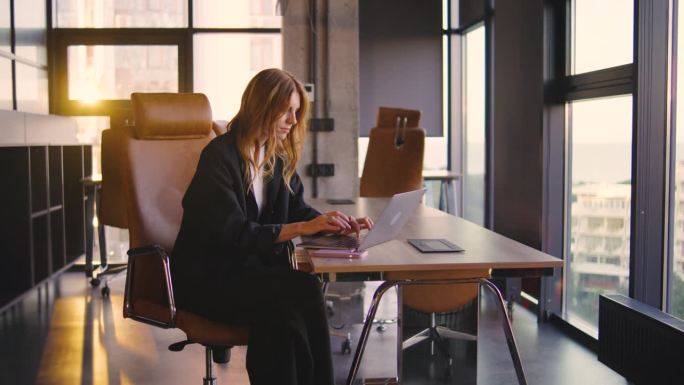 一位穿着休闲职业装的年轻专业人士在现代办公室里用一台光滑的笔记本电脑工作，捕捉着象征着创新和高生产力