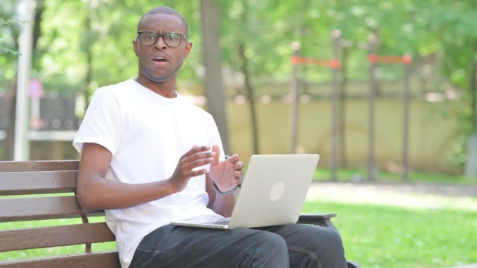 震惊的非洲年轻人在户外使用笔记本电脑时看着相机