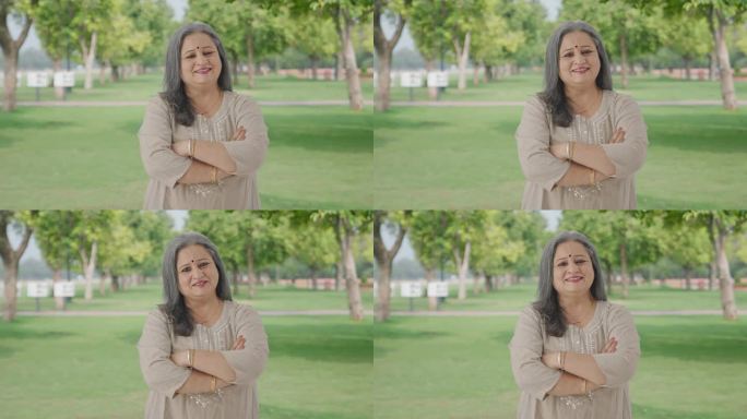 幸福的印度老妇人双手交叉站在公园里