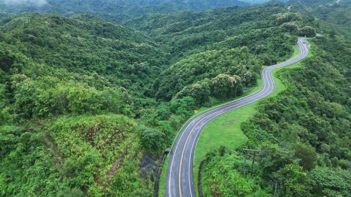 无人机在阳光下盘旋在蜿蜒的道路上，蜿蜒的柏油路穿过热带雨林。乡村景观。泰国南省的标志性旅游景点。