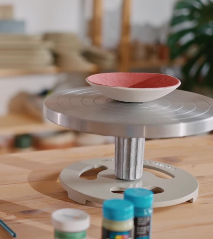 在工作室的桌子上，围绕着画笔和颜色的陶轮上的红漆陶瓷碗