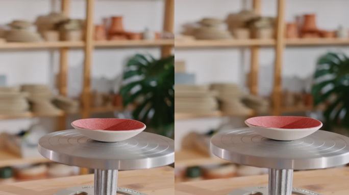 在工作室的桌子上，围绕着画笔和颜色的陶轮上的红漆陶瓷碗