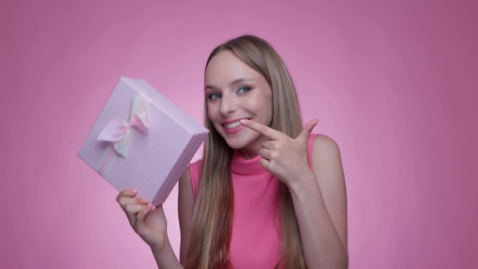 一个美丽的微笑的女孩收到了一个粉红色的盒子里的礼物，并打开了它。
