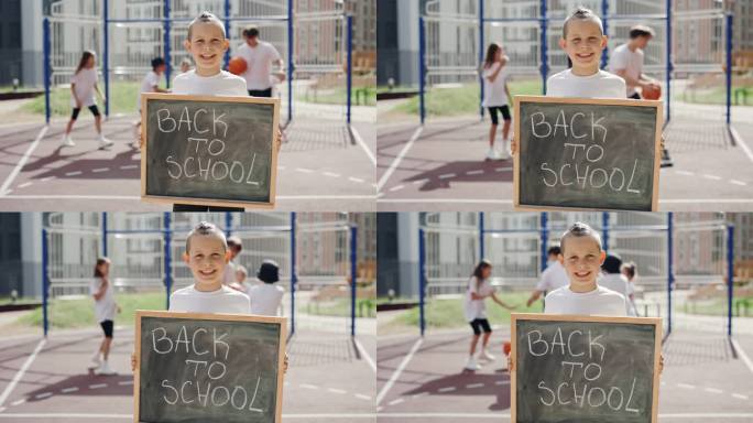 一个小男孩独自站在学校附近的街道上，举着写有文字的校董会回到学校。教育的概念。近距离