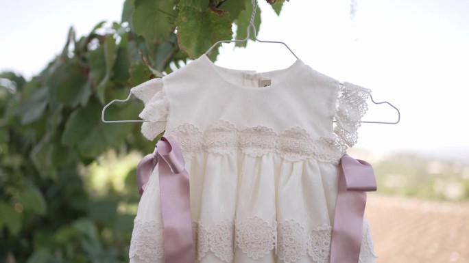 优雅的婴儿裙，蕾丝细节和粉色丝带，挂在衣架上，自然的背景，完美的洗礼或特殊场合