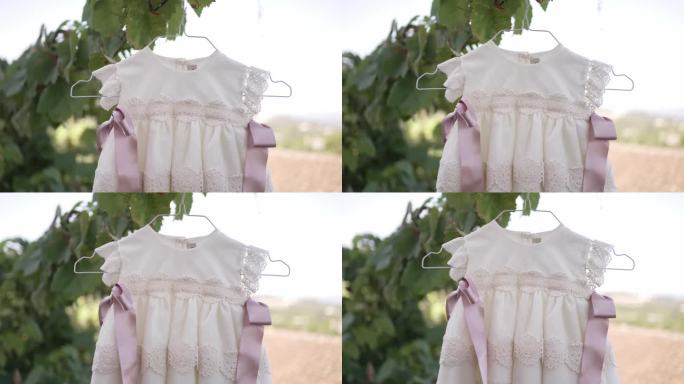 优雅的婴儿裙，蕾丝细节和粉色丝带，挂在衣架上，自然的背景，完美的洗礼或特殊场合