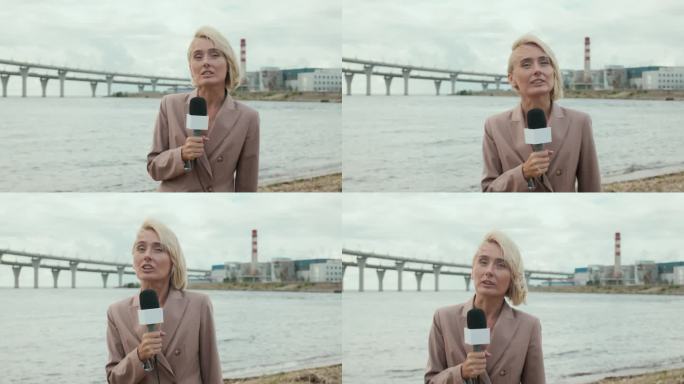 金发女子边做新闻报道边拿着麦克风走在水边