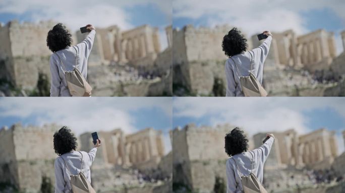 阳光明媚的一天，一名卷发女游客在阿略帕古斯山上用智能手机拍摄雅典卫城的照片