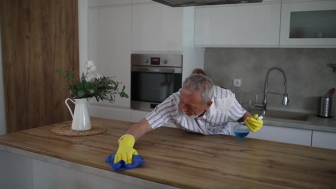 一位老人在清洁厨房柜台时，用喷雾剂清洁房子里的木制表面
