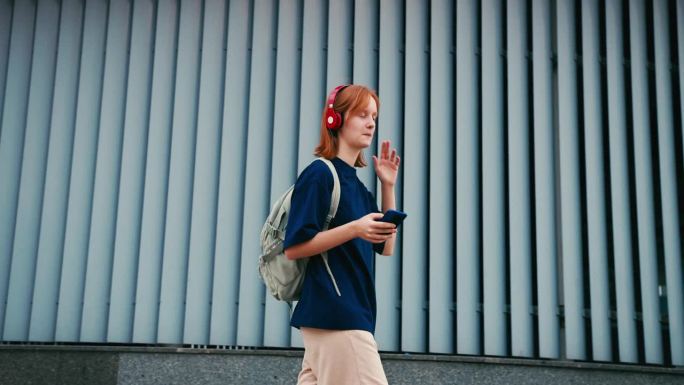 漂亮的年轻女学生背着背包和手机在户外。大学生走在大学校园里