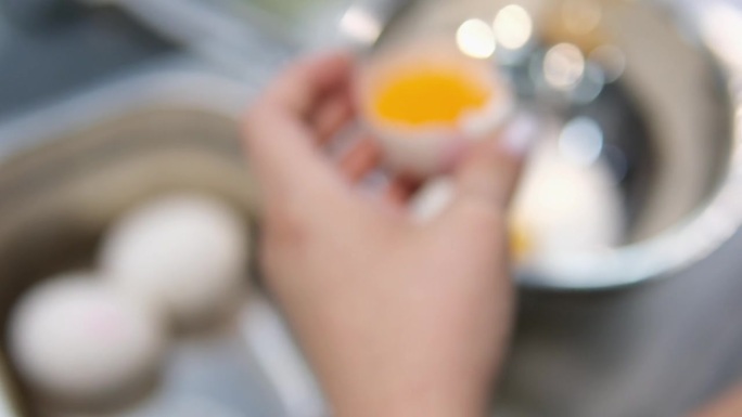 女性用手打碎鸡蛋，将背景中的蛋白、蛋黄和蛋壳分开。