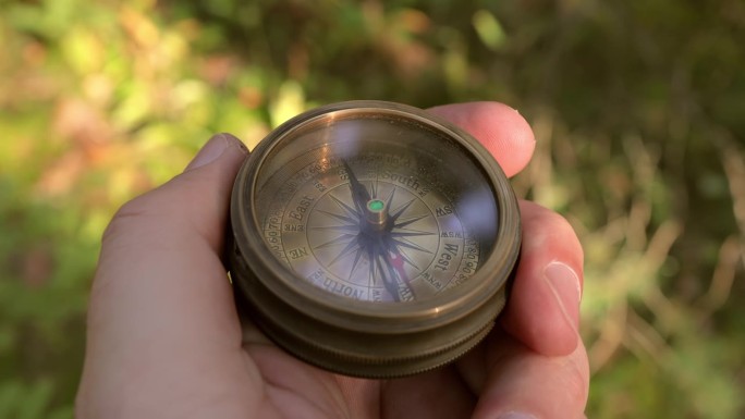 夏天的森林里，旅行者手里拿着一个古老的方向指南针。人们用指南针寻找位置。旅行概念特写。