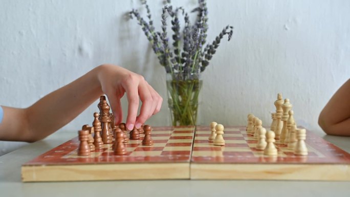 孩子的手在木板上移动棋子，以薰衣草花为背景创造了一个和平的氛围，创造了一个战略性的游戏时刻。