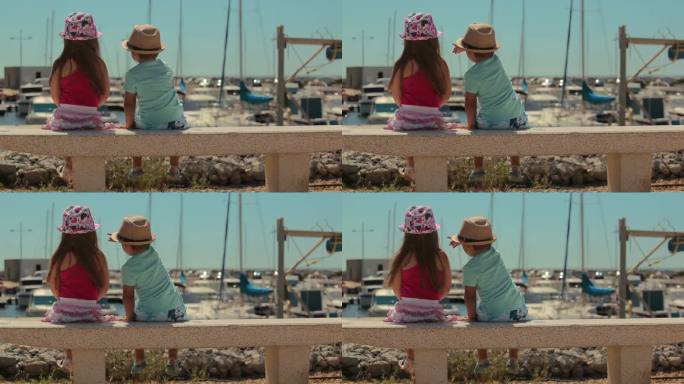 一个小男孩和一个戴着帽子的女孩在港口看游艇