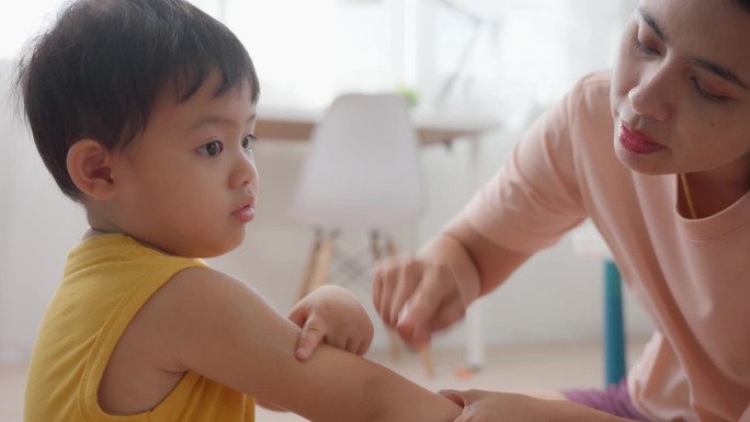 妈妈照顾他的孩子，给他涂上揉搓、驱蚊药、身体乳膏和按摩四肢部位的皮肤。