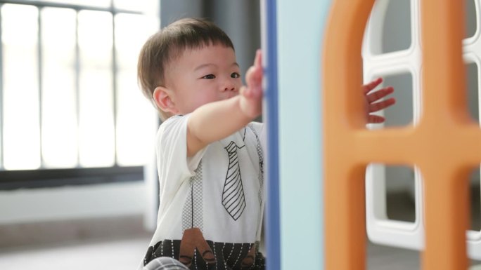 亚洲宝宝男孩爬过游戏室隧道和滑楼梯快乐快乐宝宝1岁男孩在家里客厅玩塑料房子玩具快乐在家快乐活动健康的