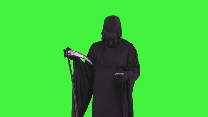 身着万圣节服装的死神手持大镰刀在绿色屏幕上用智能手机发短信