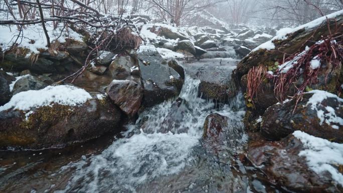 白雪覆盖的岩石和流动的水在一个宁静的冬季森林景观