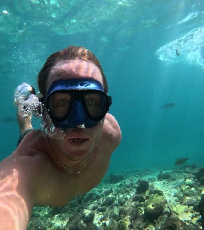 戴着水肺潜水面罩的男潜水员在海里游泳，慢动作