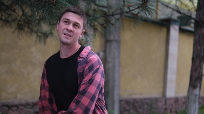 一个身穿红色格子衬衫和灰色裤子的年轻人在外面欢快地跳舞。在这组照片中，他在一面带有绿色装饰的黄墙和一