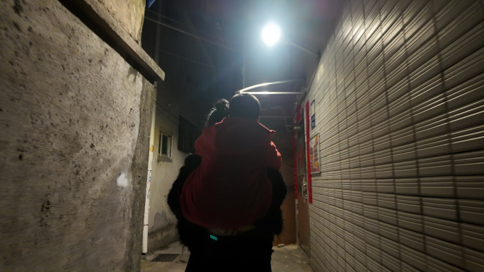 妈妈背儿子走在农村夜晚的小巷子里