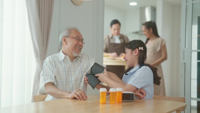 慈爱的亚洲孙女帮助爷爷测血压，家人在后台准备饭菜