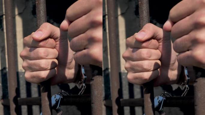 垂直:一名囚犯握紧金属笼子的铁栏。囚禁的概念。犯了罪。监禁，被囚禁的军人。被铐在笼子里
