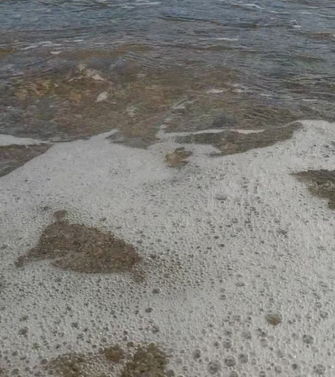 竖屏视频，镜头向前移动，低角度拍摄卵石海滩和逼近的海浪，慢动作。