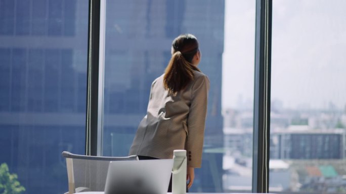 年轻女性在现代办公室用笔记本电脑工作时伸展身体。